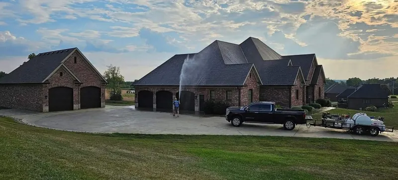 Brian Meyer soft washing the roof of a brick estate home from the ground, with the Meyer Pressure Washing truck and trailer in the driveway